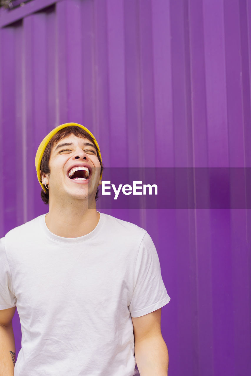 Cheerful non-binary person laughing in front of purple wall