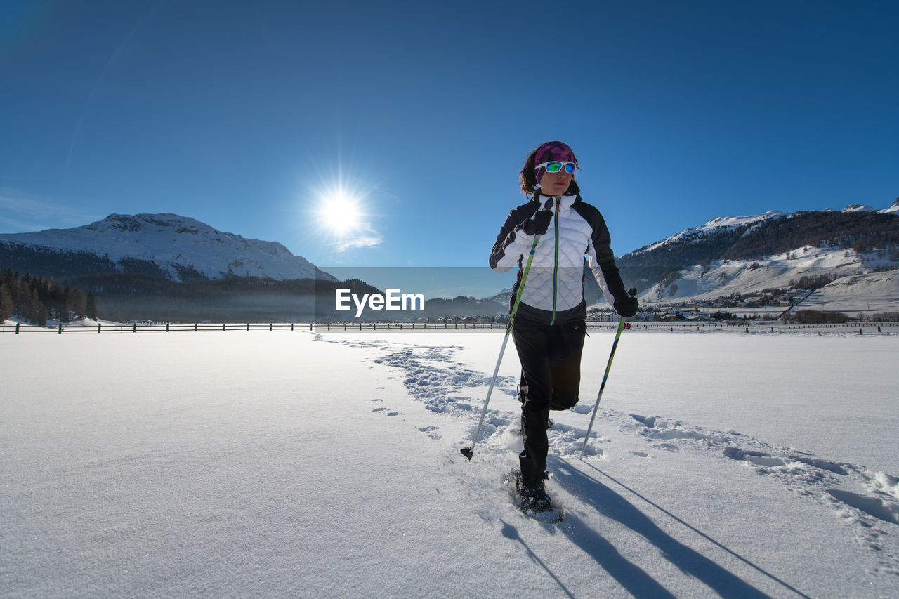 WOMAN STANDING ON SNOWCAPPED MOUNTAIN AGAINST SKY