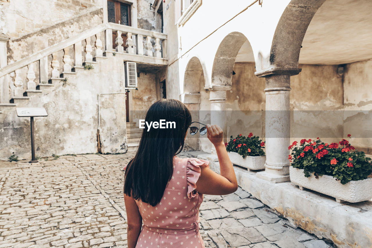 Young woman in summer dress putting on sunglasses.