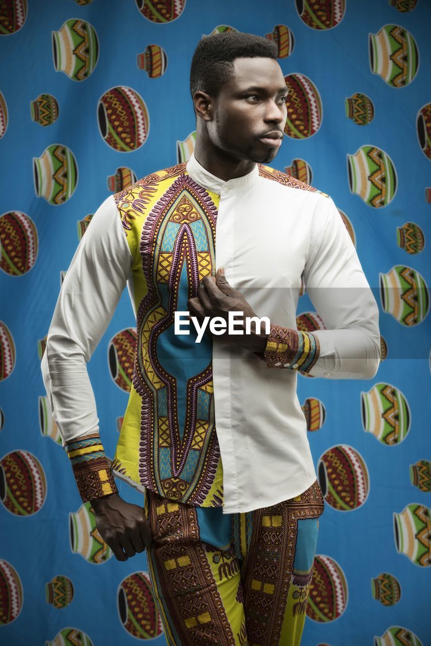 Young man wearing patterned clothing standing against multi colored background
