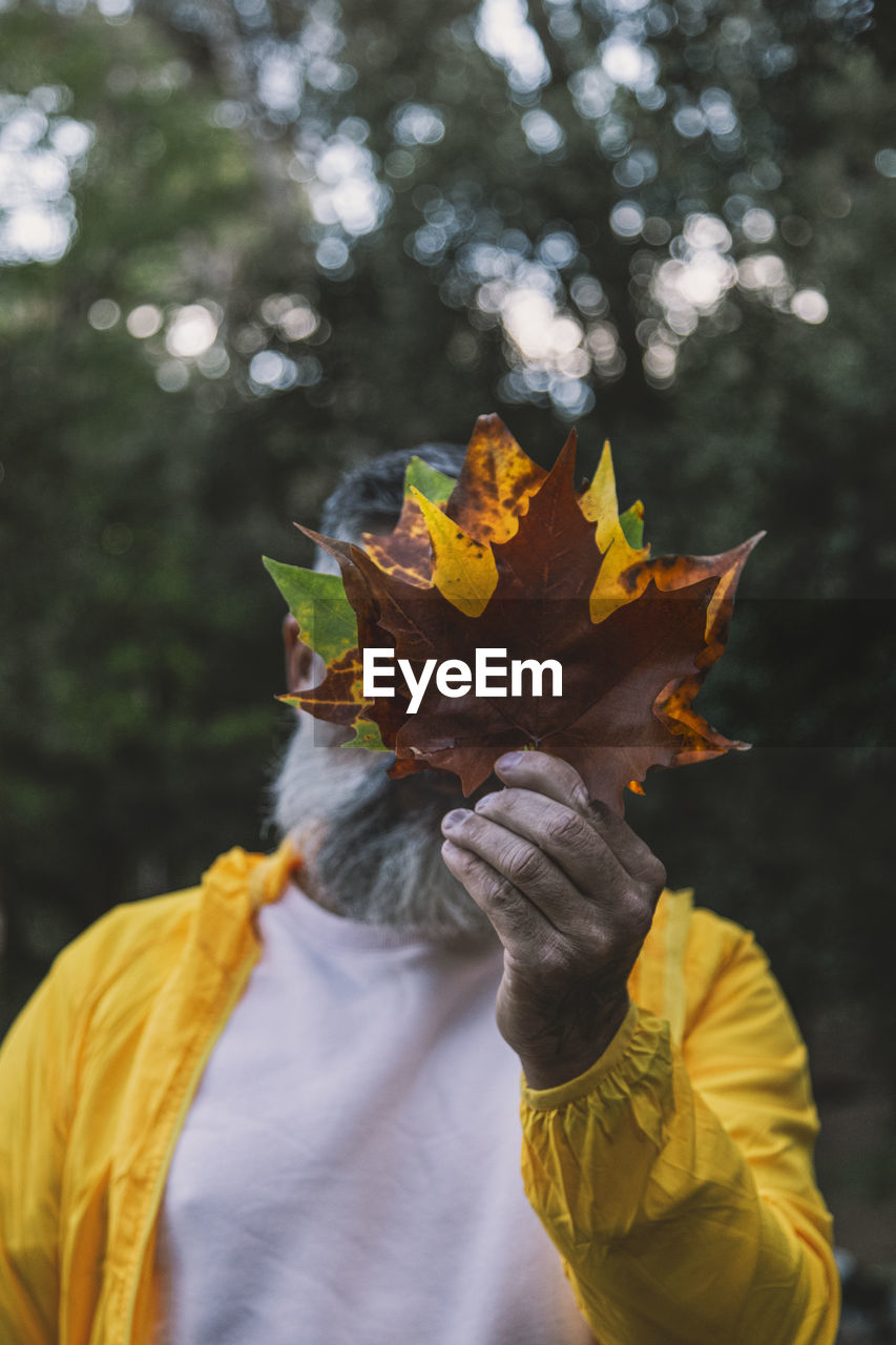 Man holding autumn leaf in front face person