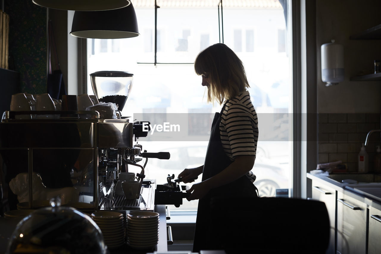 Side view of female barista preparing coffee by window at cafe