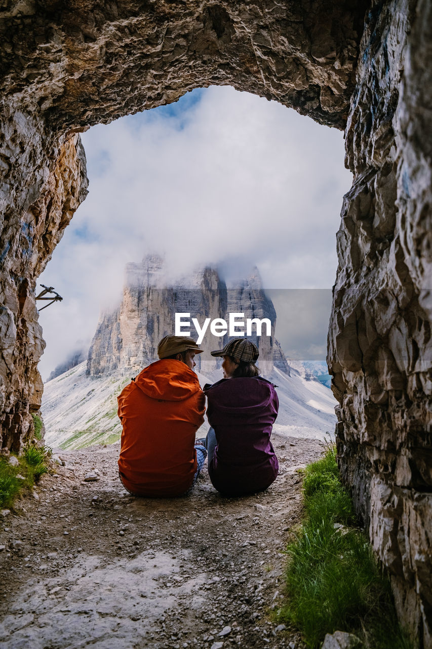 REAR VIEW OF PEOPLE SITTING ON ROCK