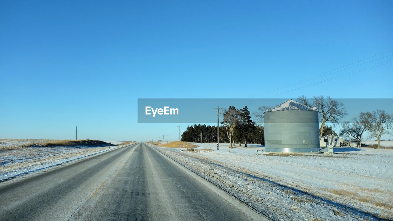 Empty road by field against blue sky during winter