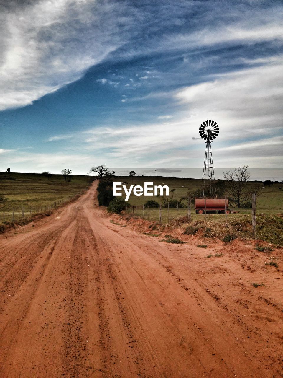 Dirt road amidst field against sky