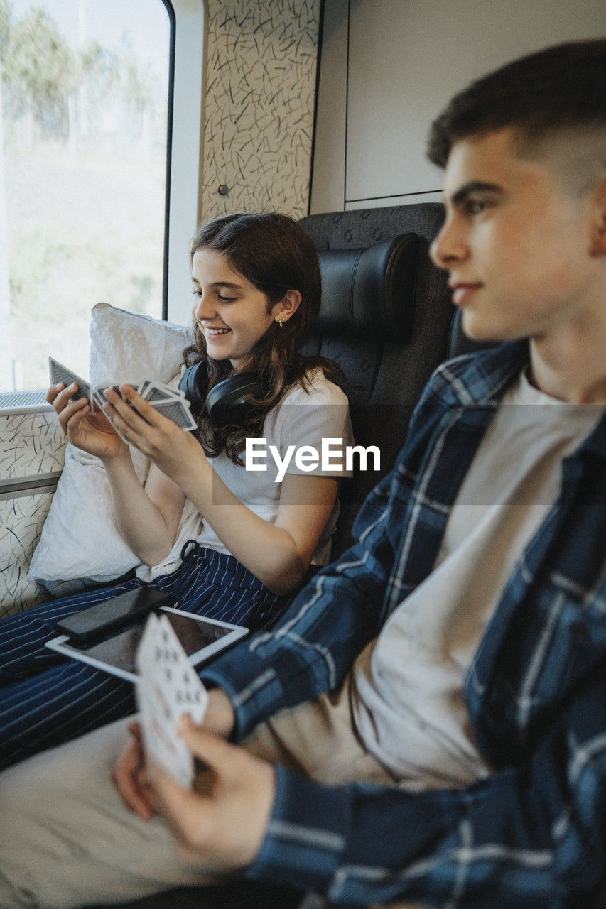 Smiling girl playing cards while sitting next to brother in train