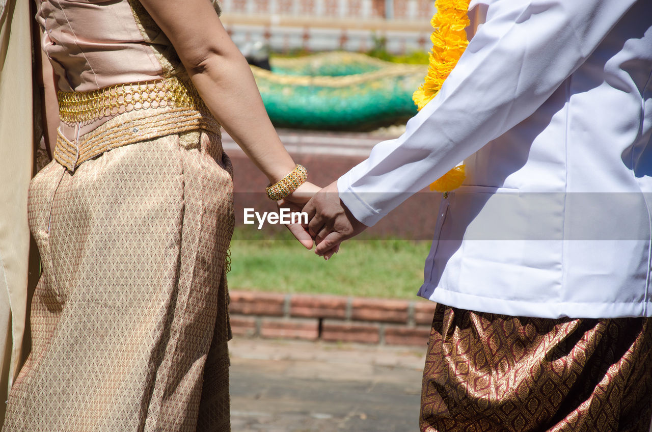 Midsection of couple holding hands while standing on footpath