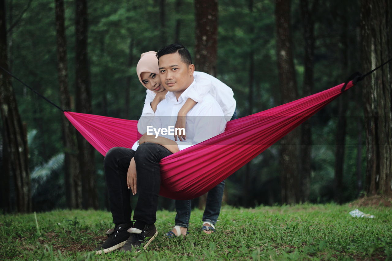 Portrait of woman with boyfriend sitting on hammock in forest