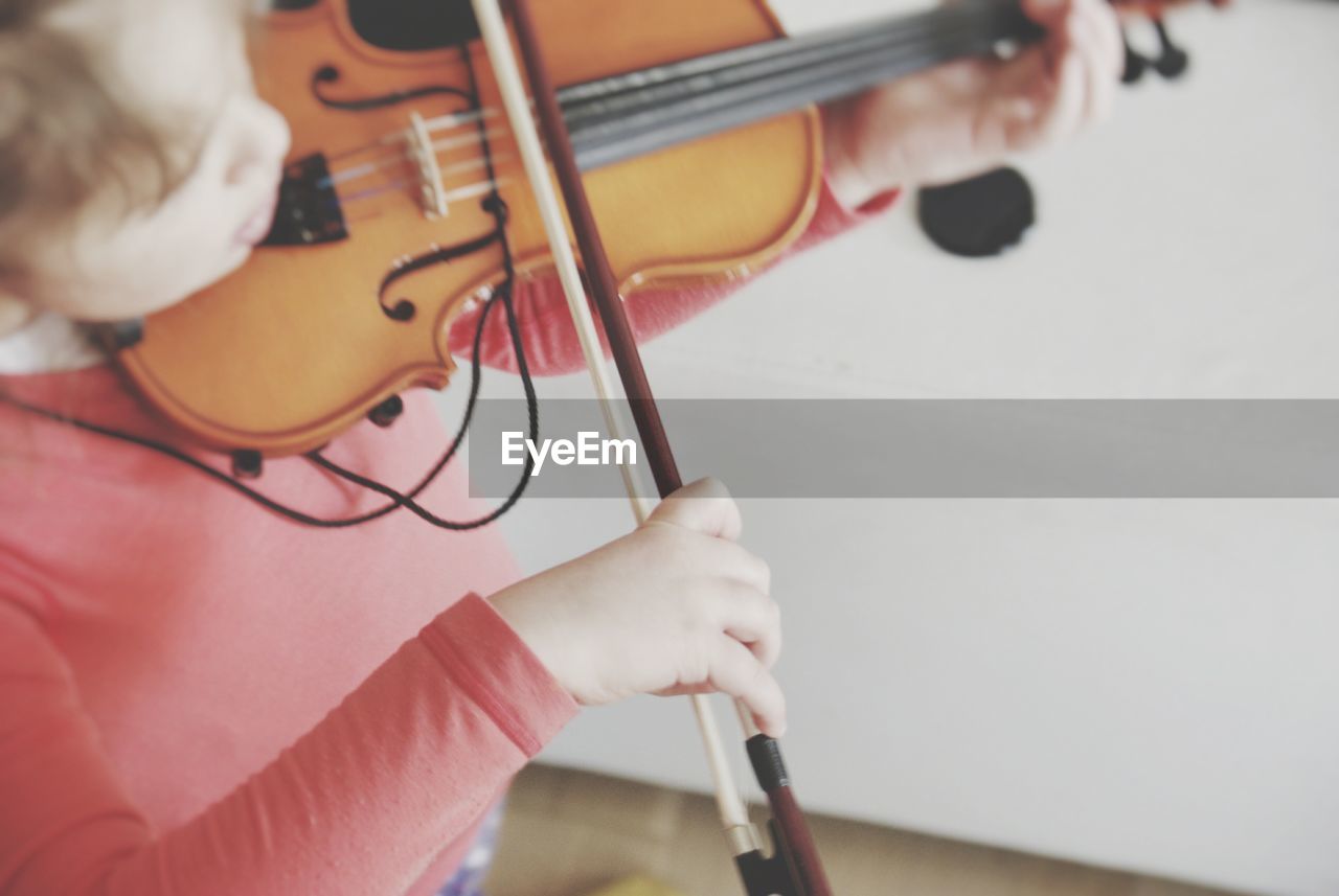 High angle view of girl playing violin by wall at home