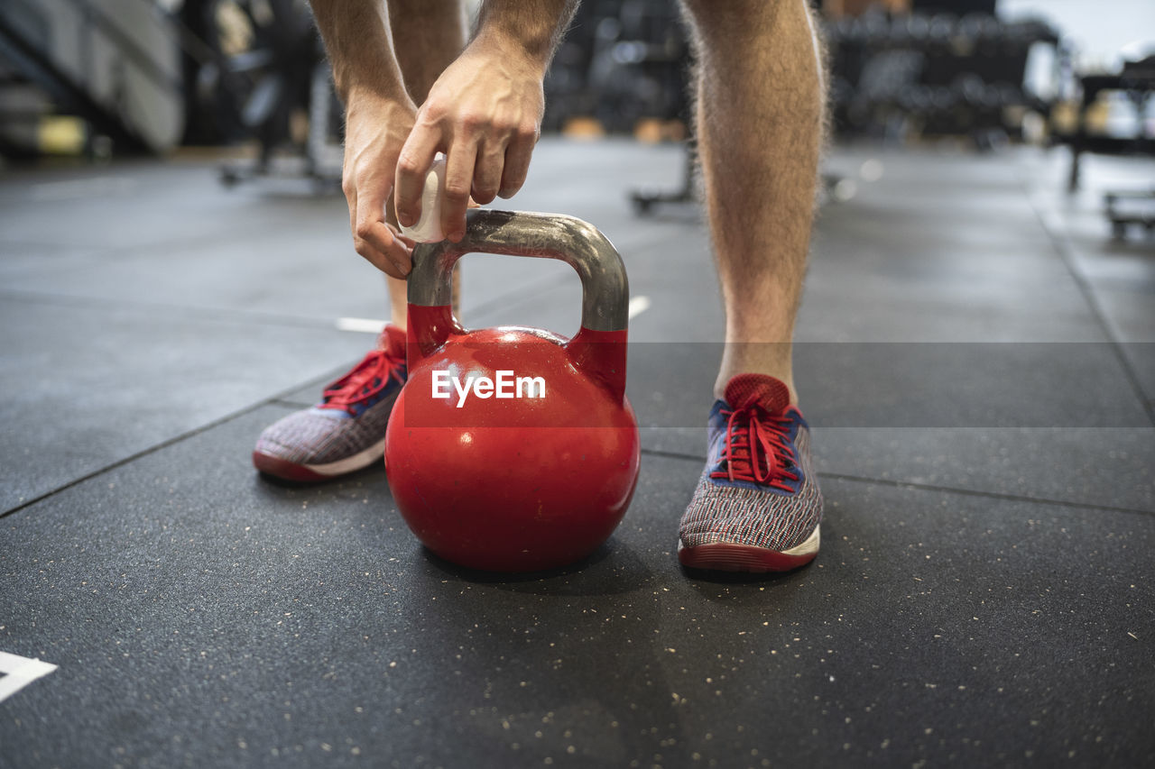 Legs of man holding kettlebell while standing in gym