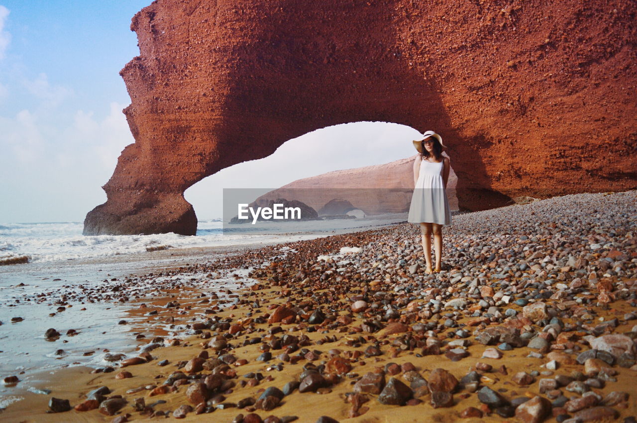 Full length of woman standing against rock formation at beach