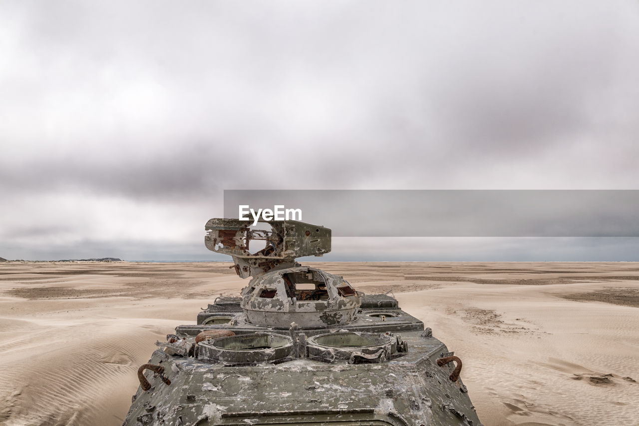 Abandoned armored tank at desert against cloudy sky