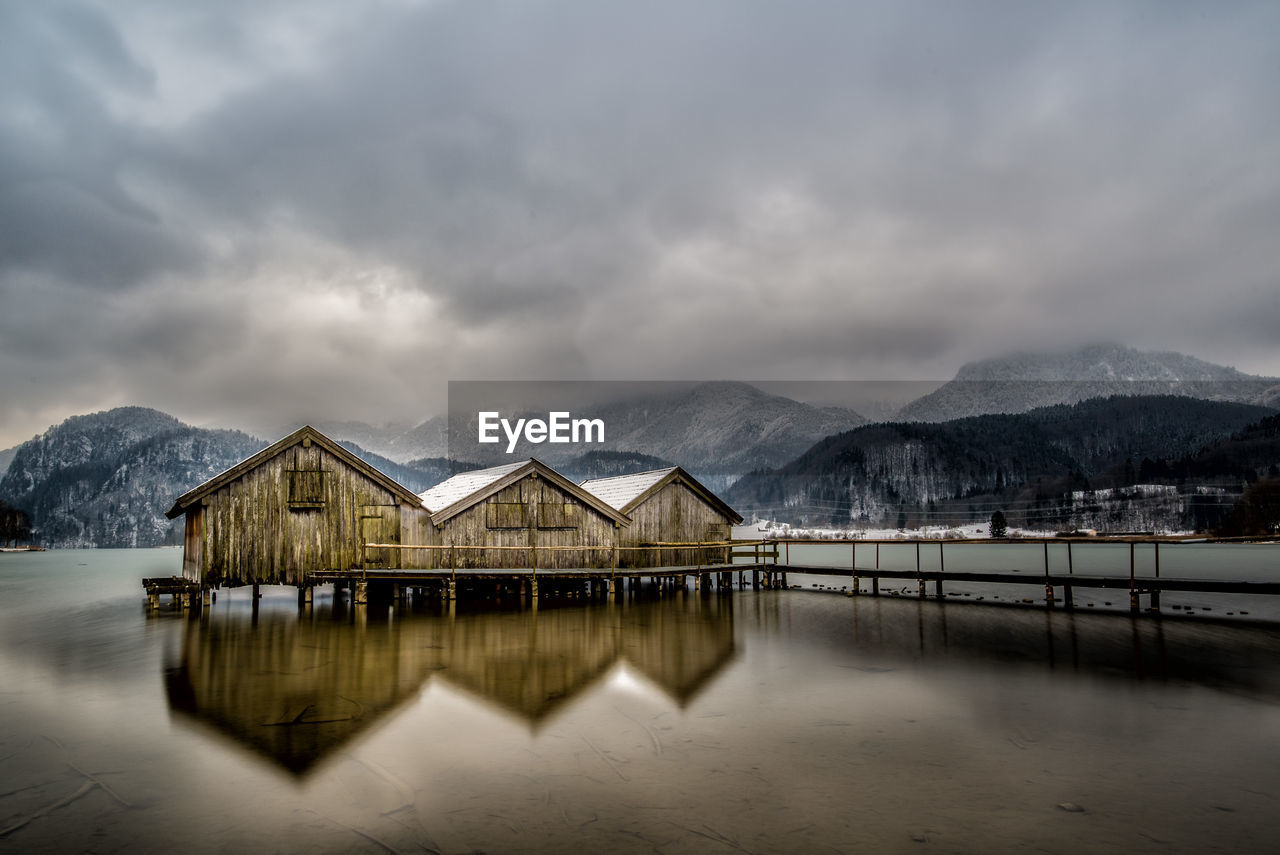 House by lake and mountains against sky