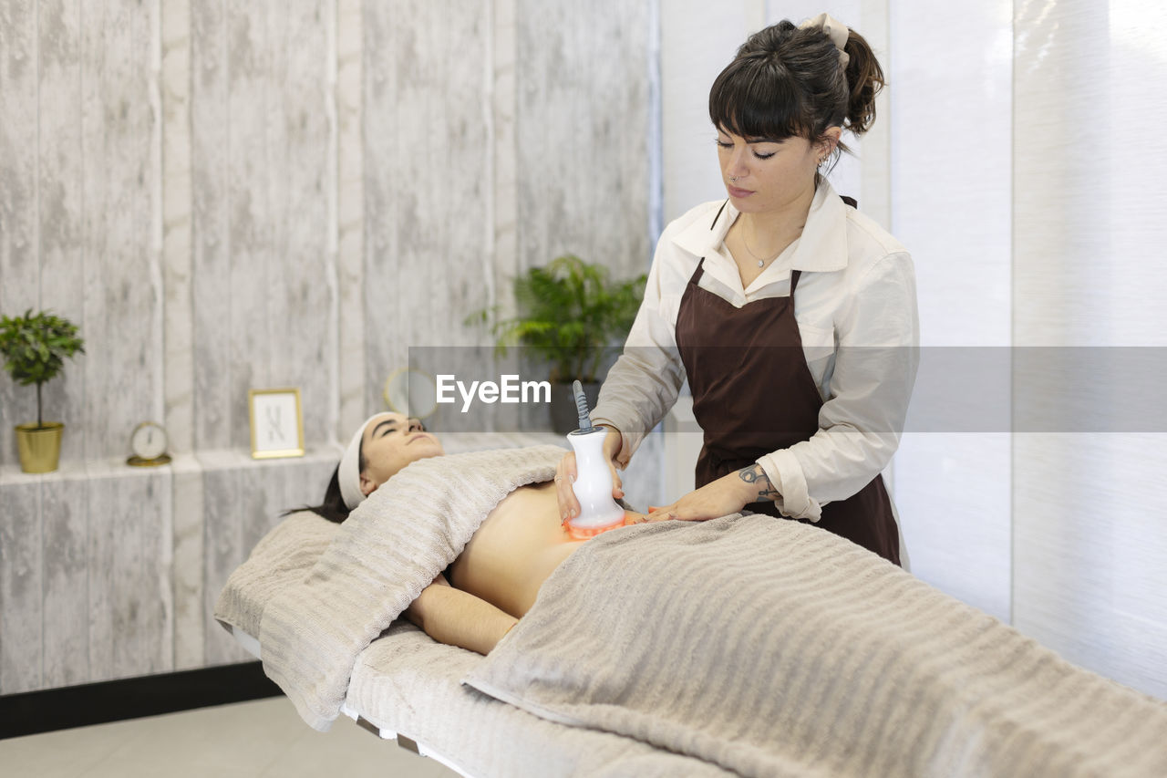 Therapist giving massage to woman with tool at aesthetic clinic