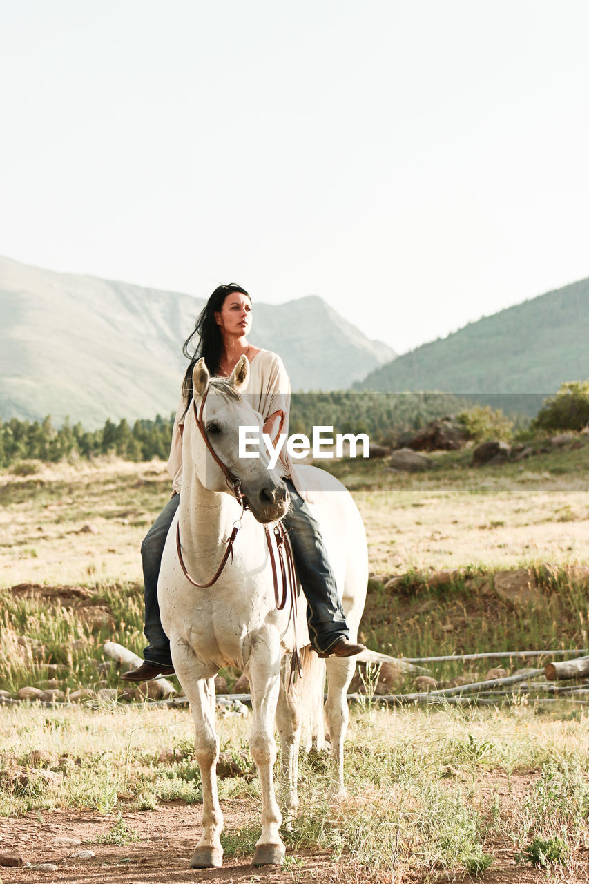 Woman horseback riding on grassy field against clear sky