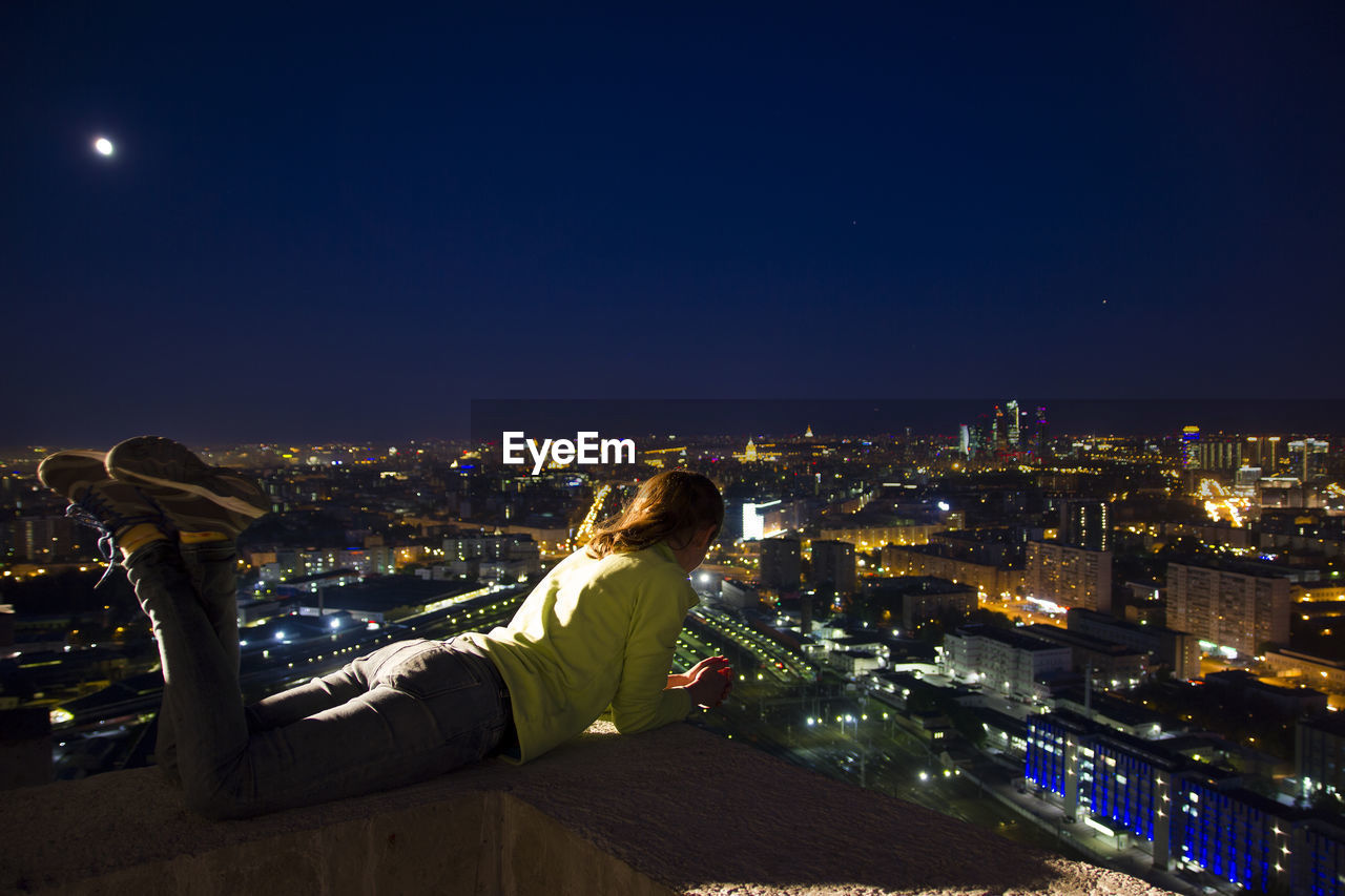 Woman lying on terrace in illuminated city at night