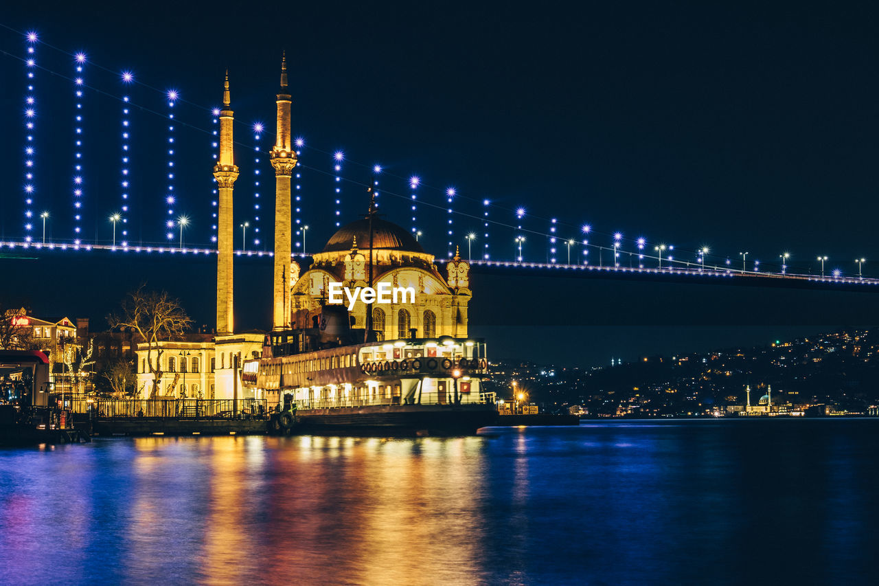 Illuminated ortakoy mosque with bridge in background in istanbul at night