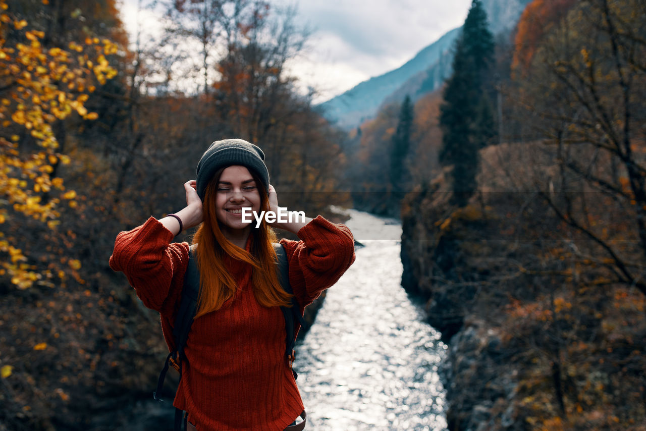 YOUNG WOMAN STANDING AGAINST TREES DURING WINTER