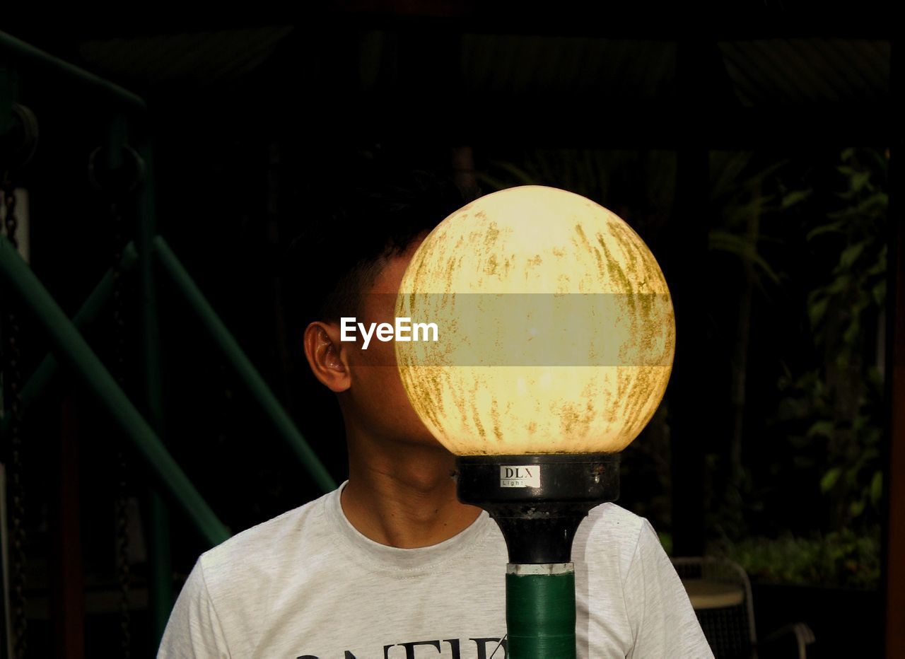 Close-up of man by illuminated lamp post at night