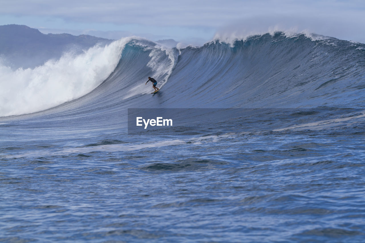 Man surfing on waves at sea against sky