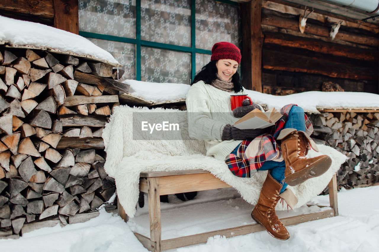 Woman in warm clothing reading book sitting on bench