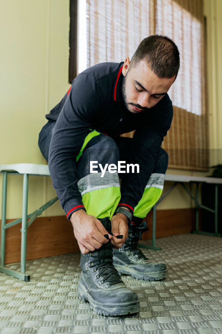 Seated firefighter buckling his boots before starting work in the metal-floored men's locker room