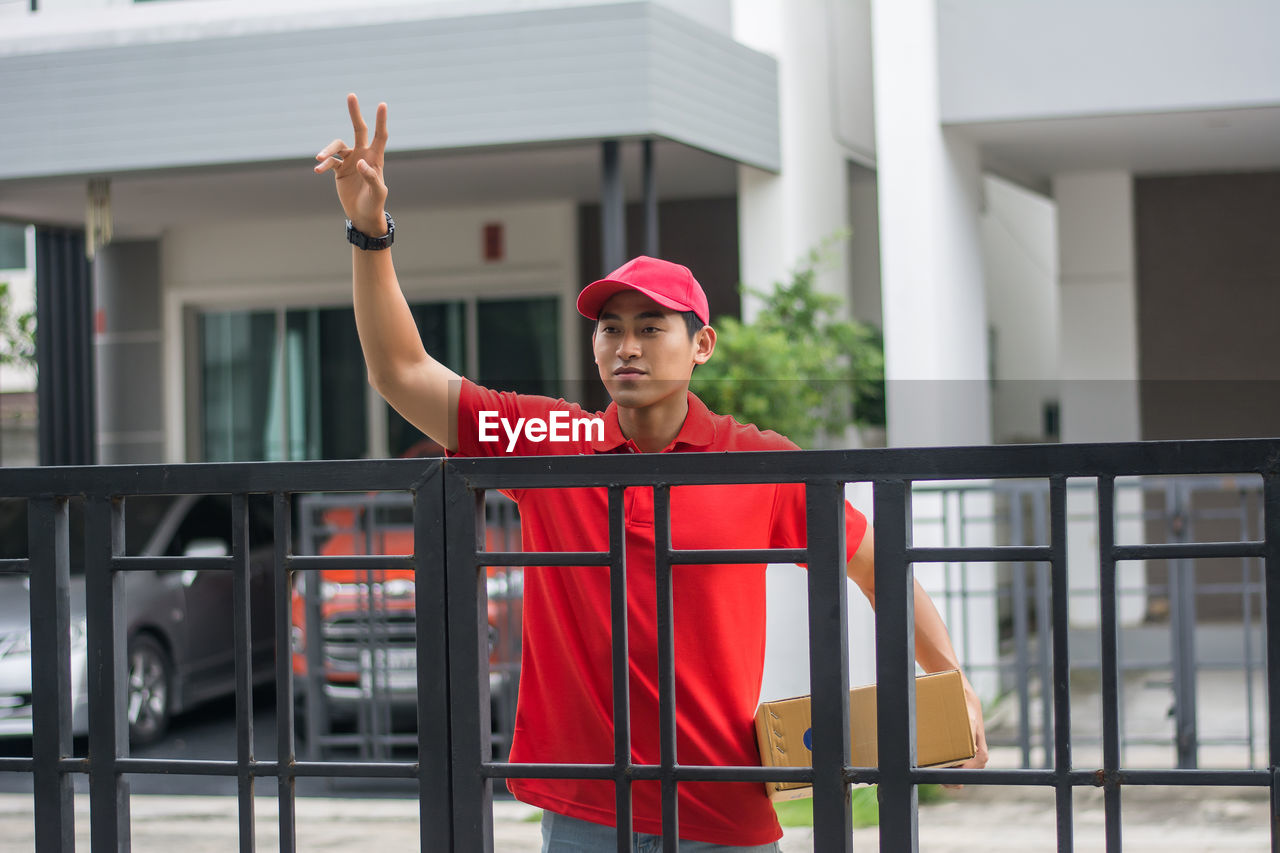 Delivery man standing at closed gate against buildings