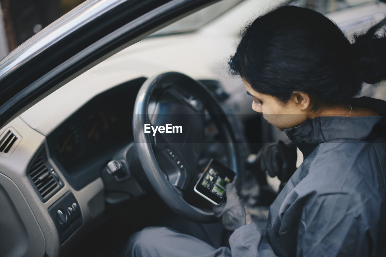 Female mechanic using mobile phone while sitting in car