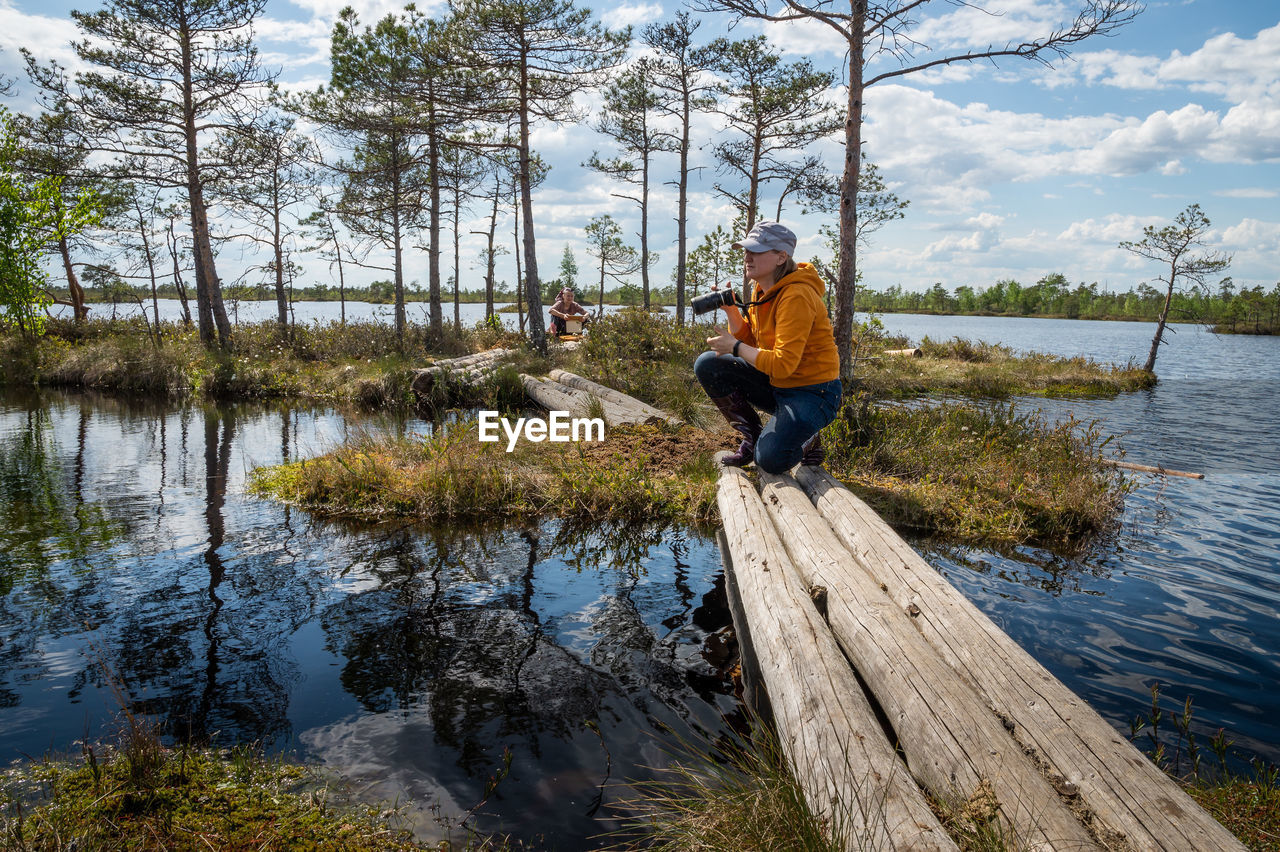 A woman with a camera sat down on a wooden walkway leading from the shore to an island on the lake