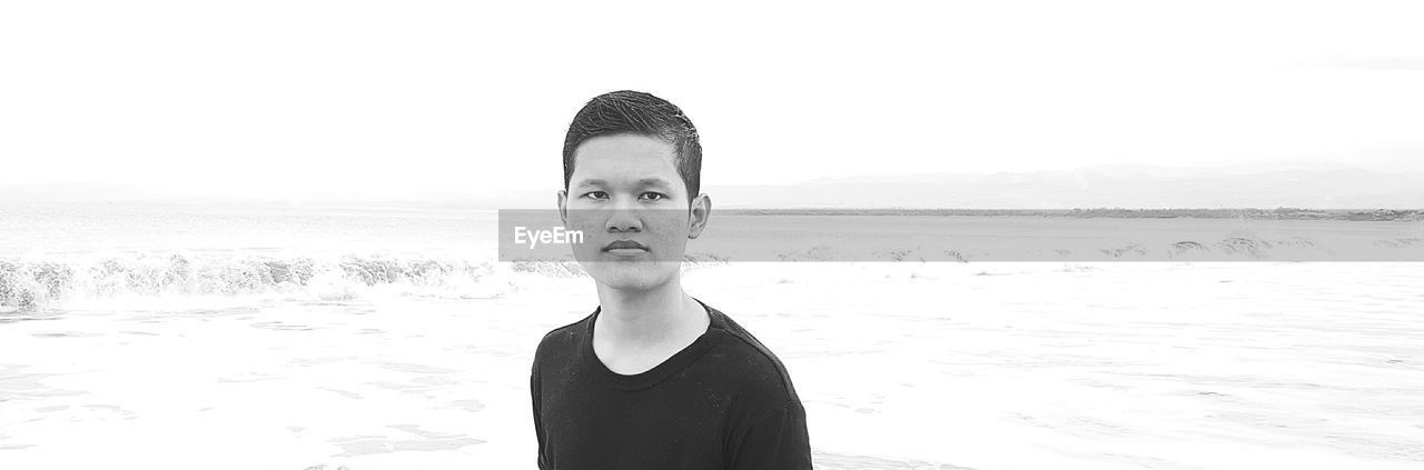 PORTRAIT OF YOUNG MAN STANDING AT BEACH