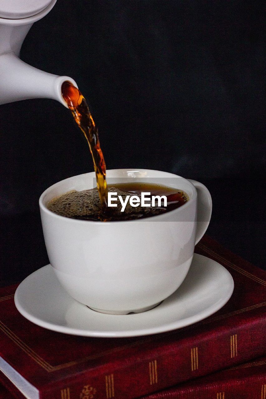 Pouring coffee into cup on black background