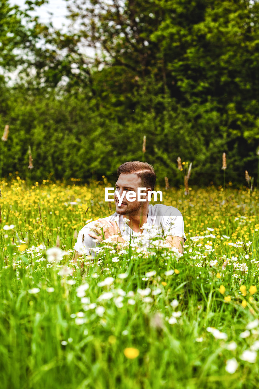 Smiling man looking away while sitting by plants