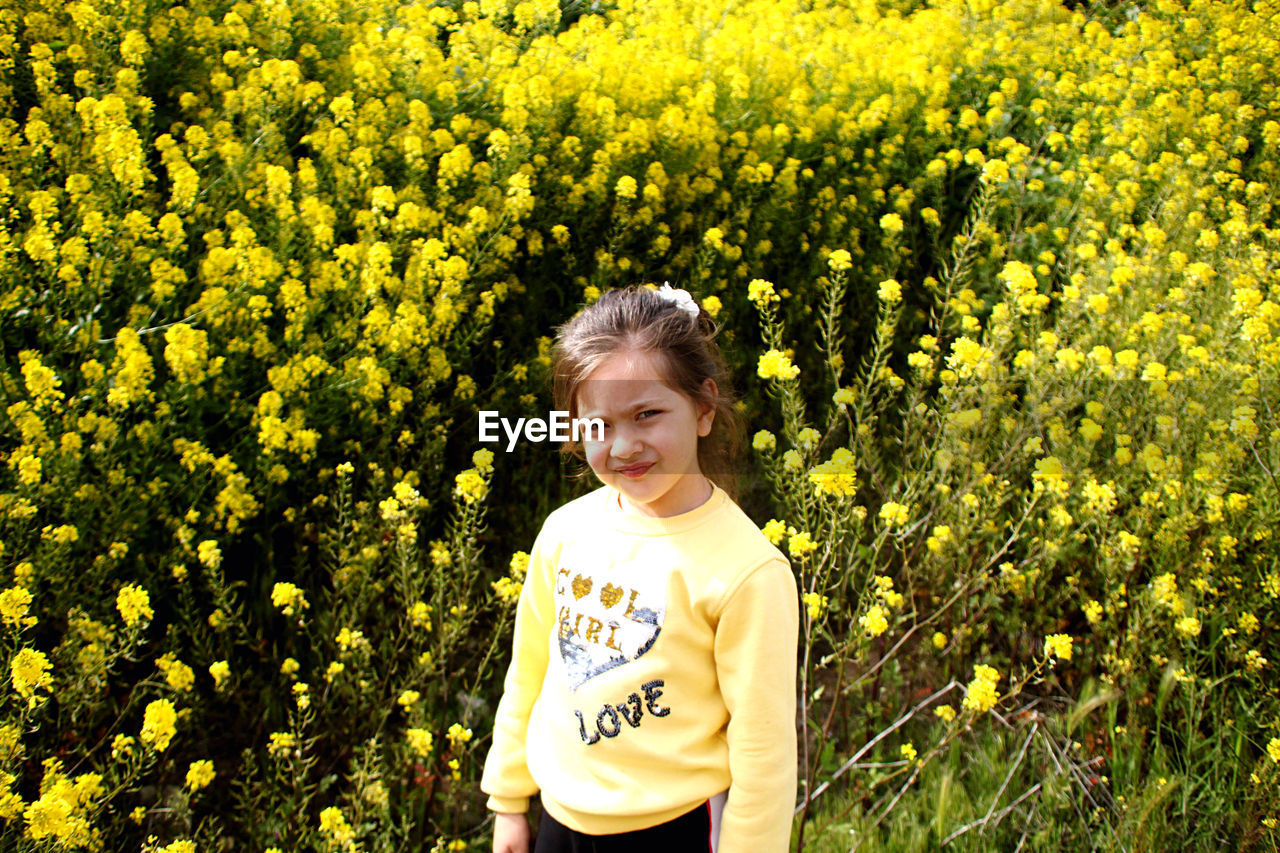 Portrait of girl standing against yellow flowers blooming on field