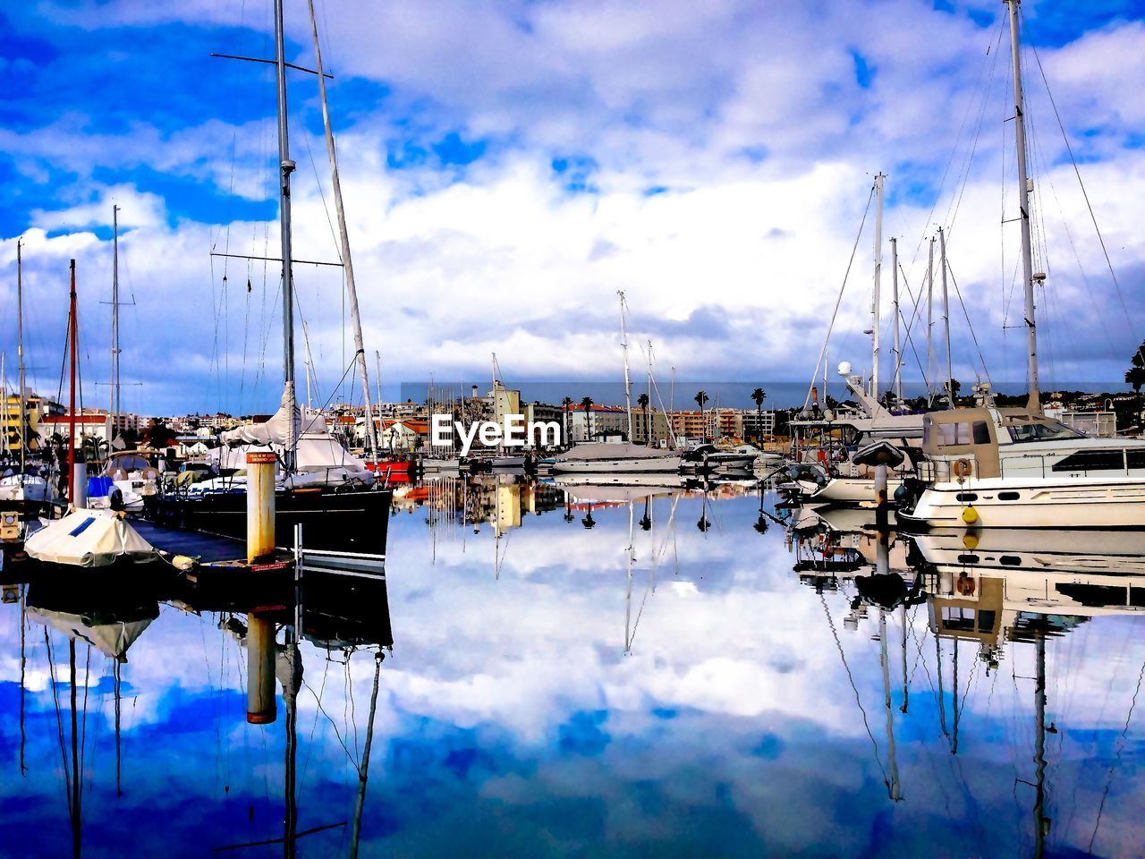 SAILBOATS MOORED AT HARBOR BY MOUNTAINS AGAINST SKY