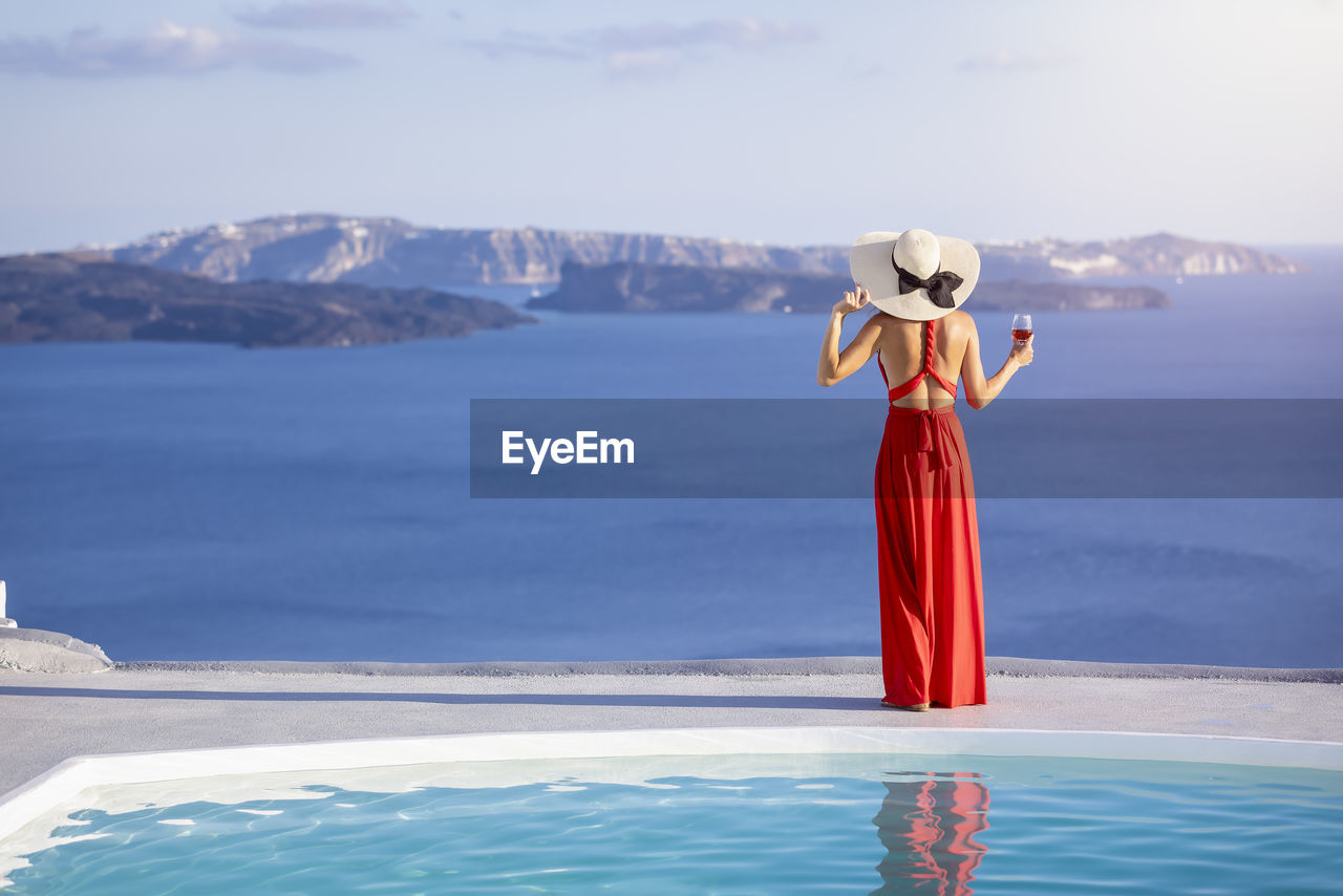 Rear view of woman holding drink looking at sea