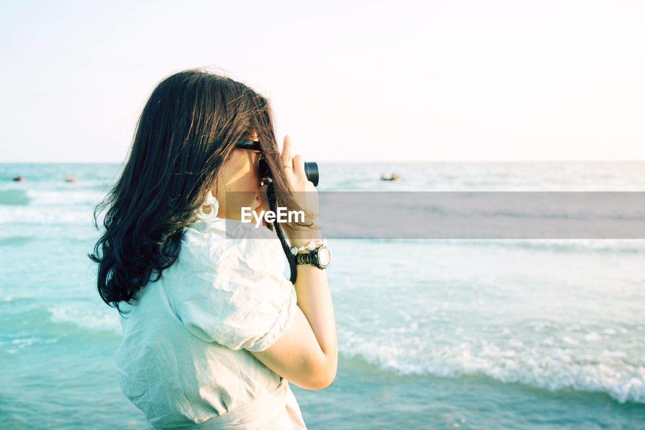 Close-up of woman photographing while standing at beach against sky