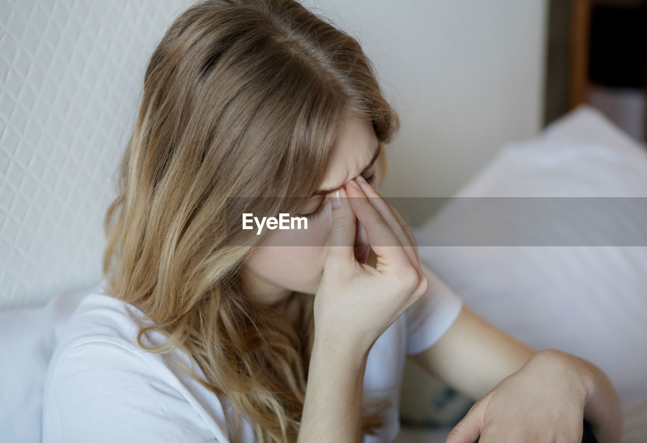 Young woman suffering from headache sitting on bed at home