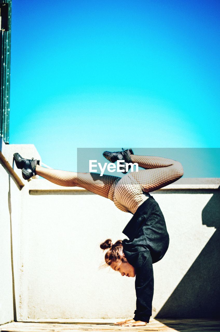 Full length of ballet dancer performing dance against clear blue sky on sunny day