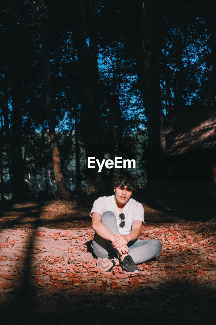 Young man sitting on dry leaves against trees in forest