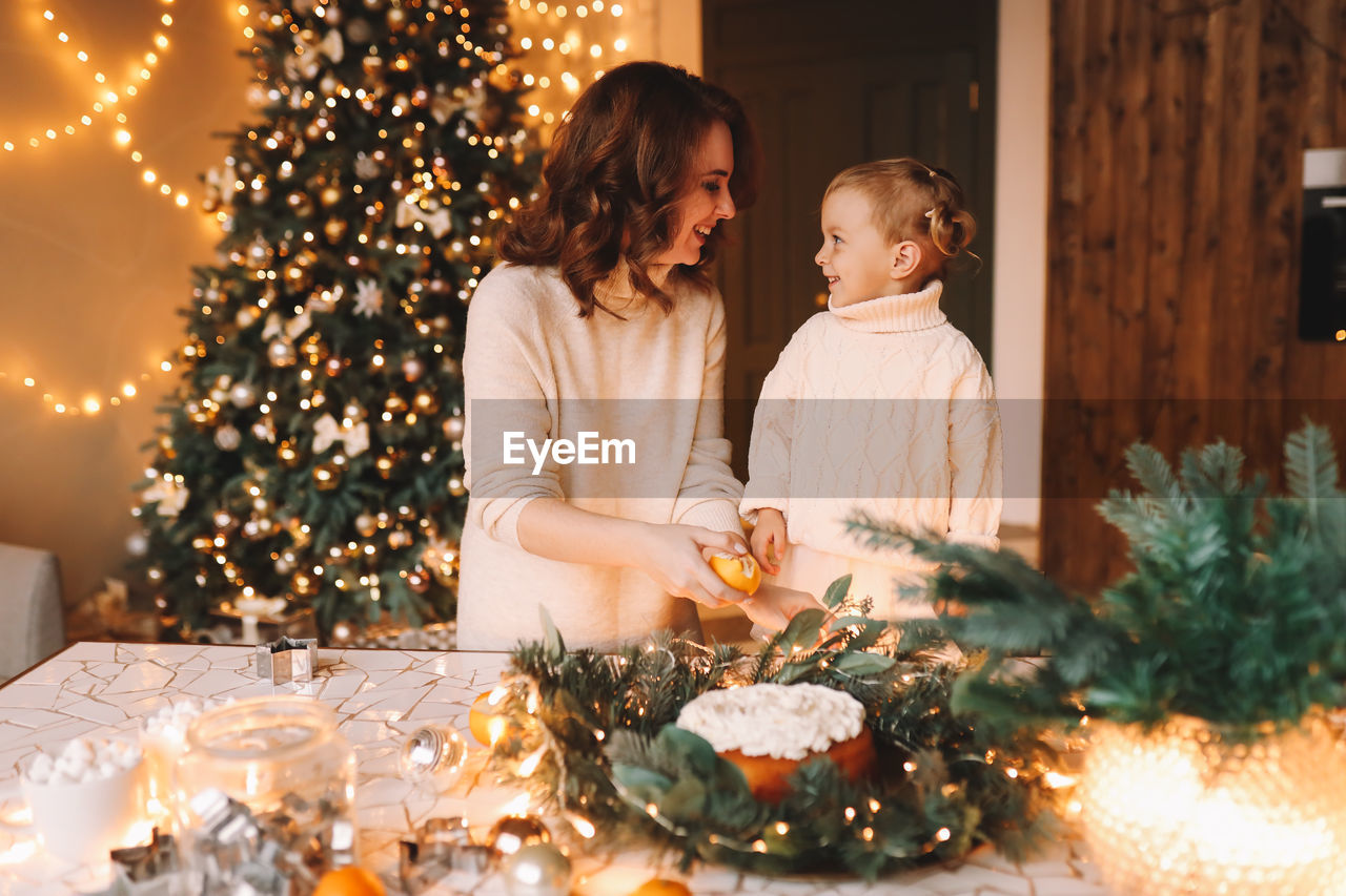 Happy mom and daughter in sweaters together prepare cake for christmas holiday in kitchen at home