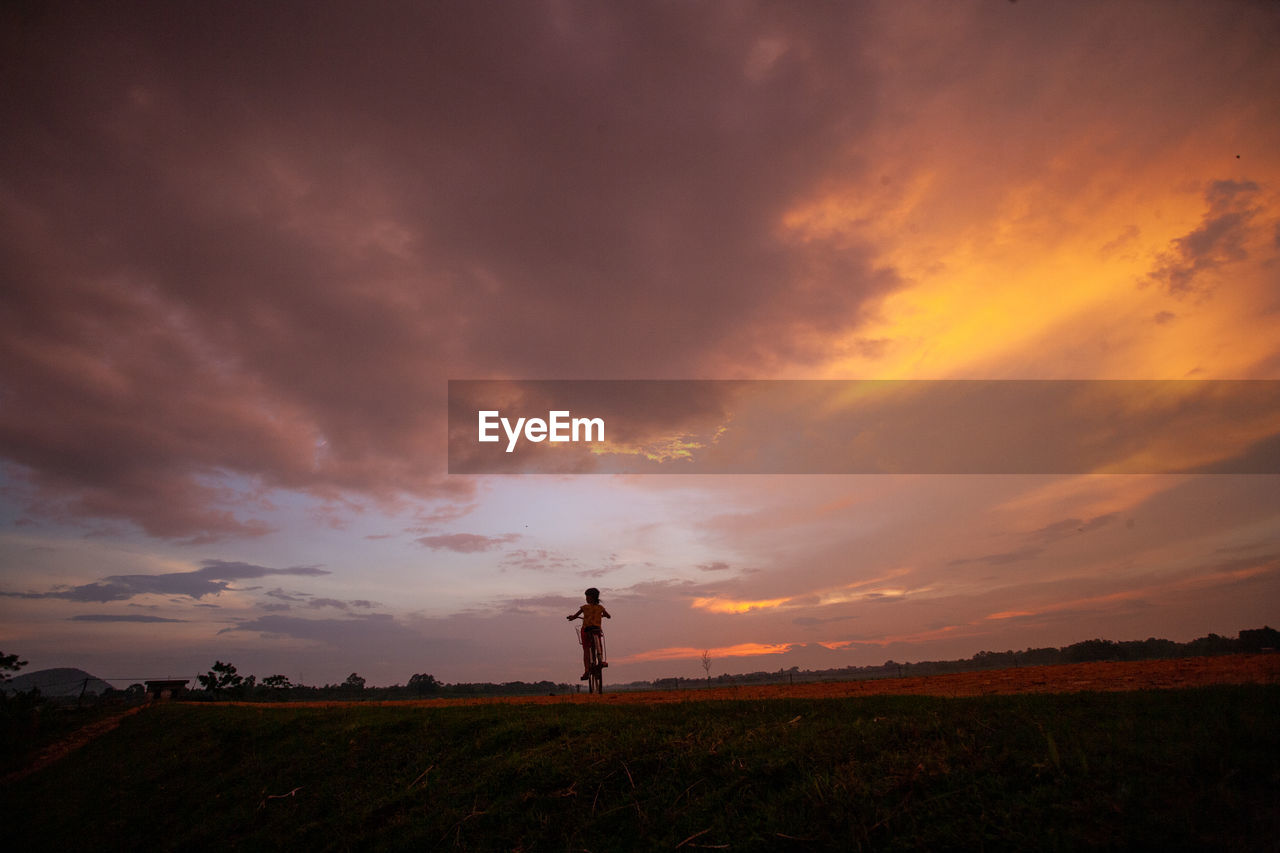 Silhouette person standing on field against sky during sunset