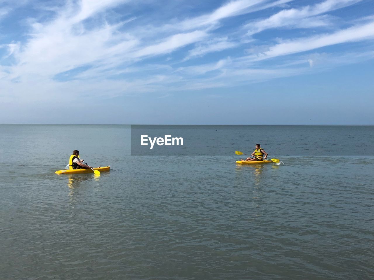 Boys kayaking on sea against sky