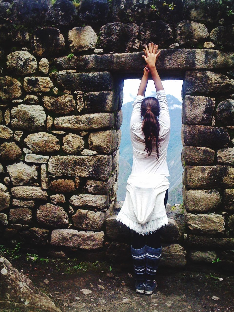 Rear view of women looking at scenic view of nature through gap of stone wall 