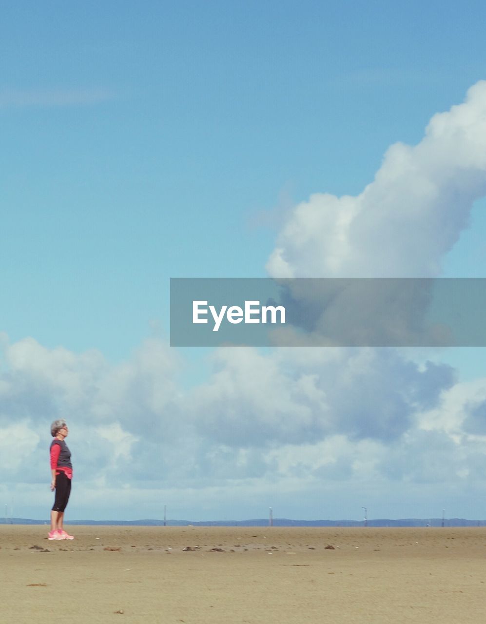 Side view of woman standing at beach against cloudy sky