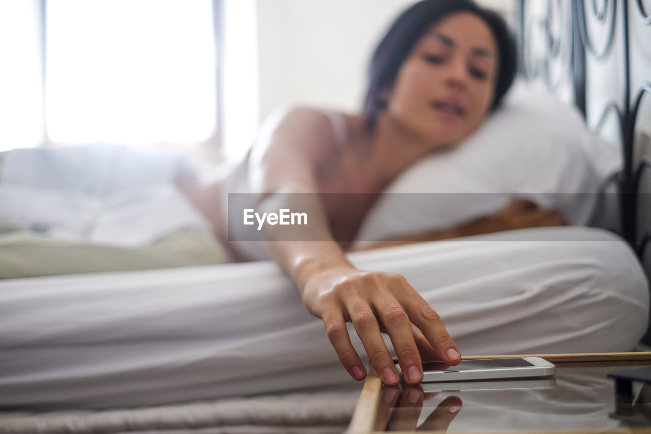 Young woman in bed, taking smartphone