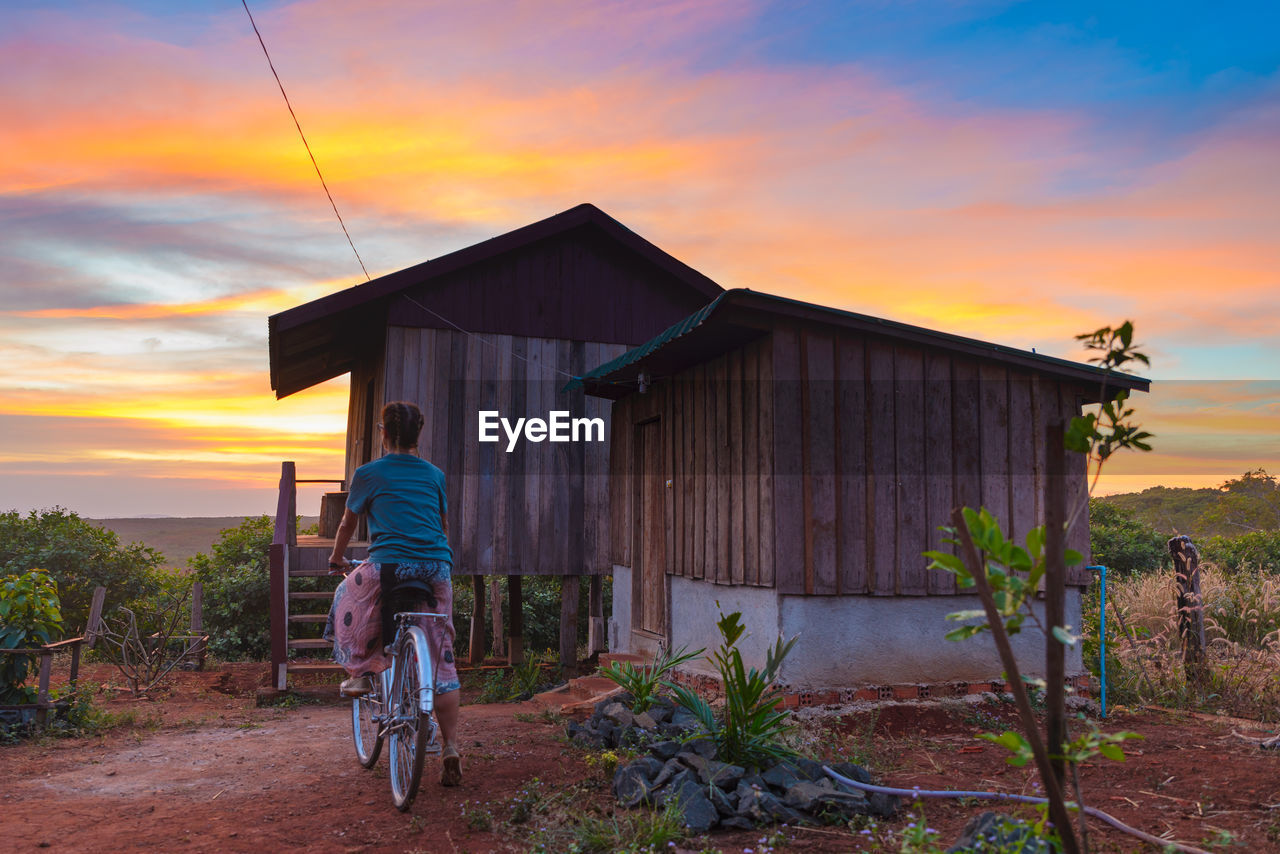 REAR VIEW OF MAN CYCLING AGAINST ORANGE SKY