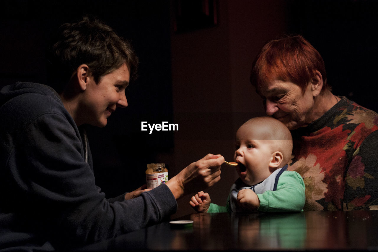 Portrait of mother feeding baby boy on grannys lap