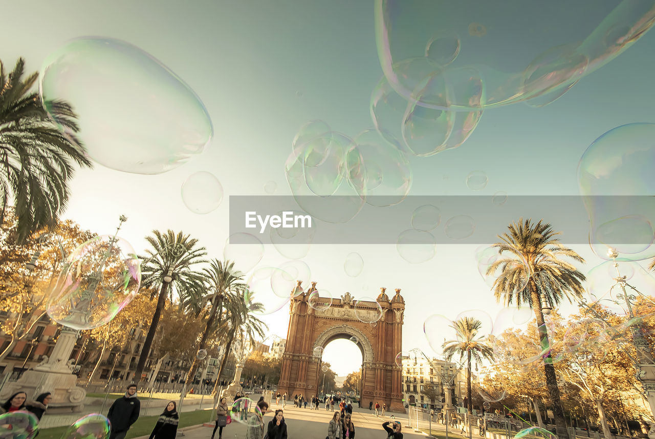 Tilt image of people playing with soap bubbles at arc de triomf against sky