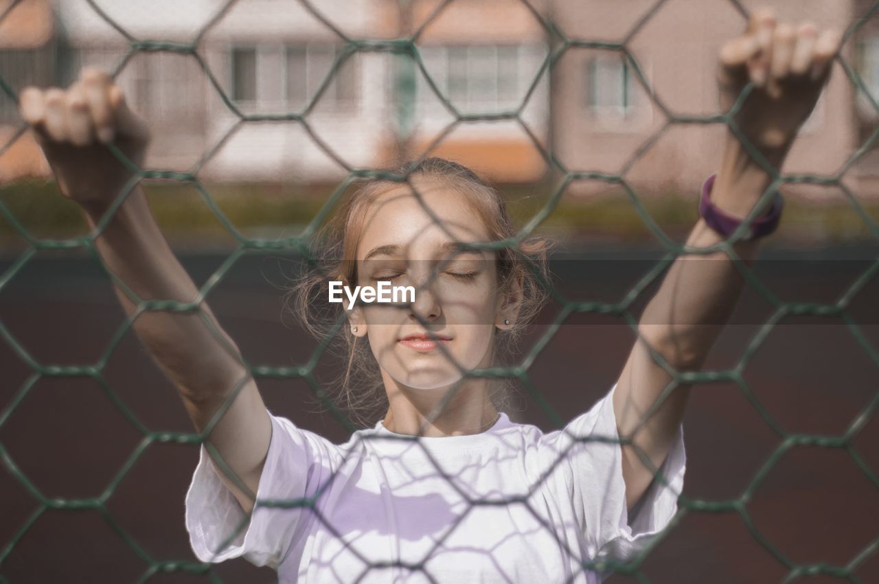 Girl with closed eyes seen through chainlink fence