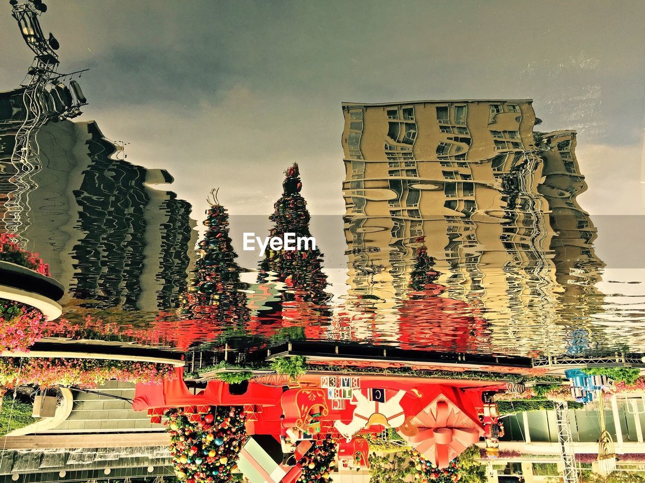 Reflection of buildings with christmas tree against sky in puddle